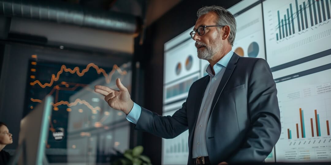 Business professional presenting a financial report with data visualizations on large screens in the background.